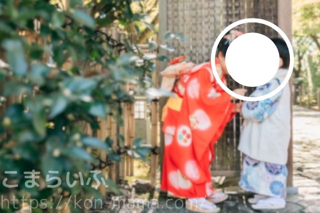 七五三で赤と水色の着物を着た姉妹が、神社の門の前で寄り添う様子。